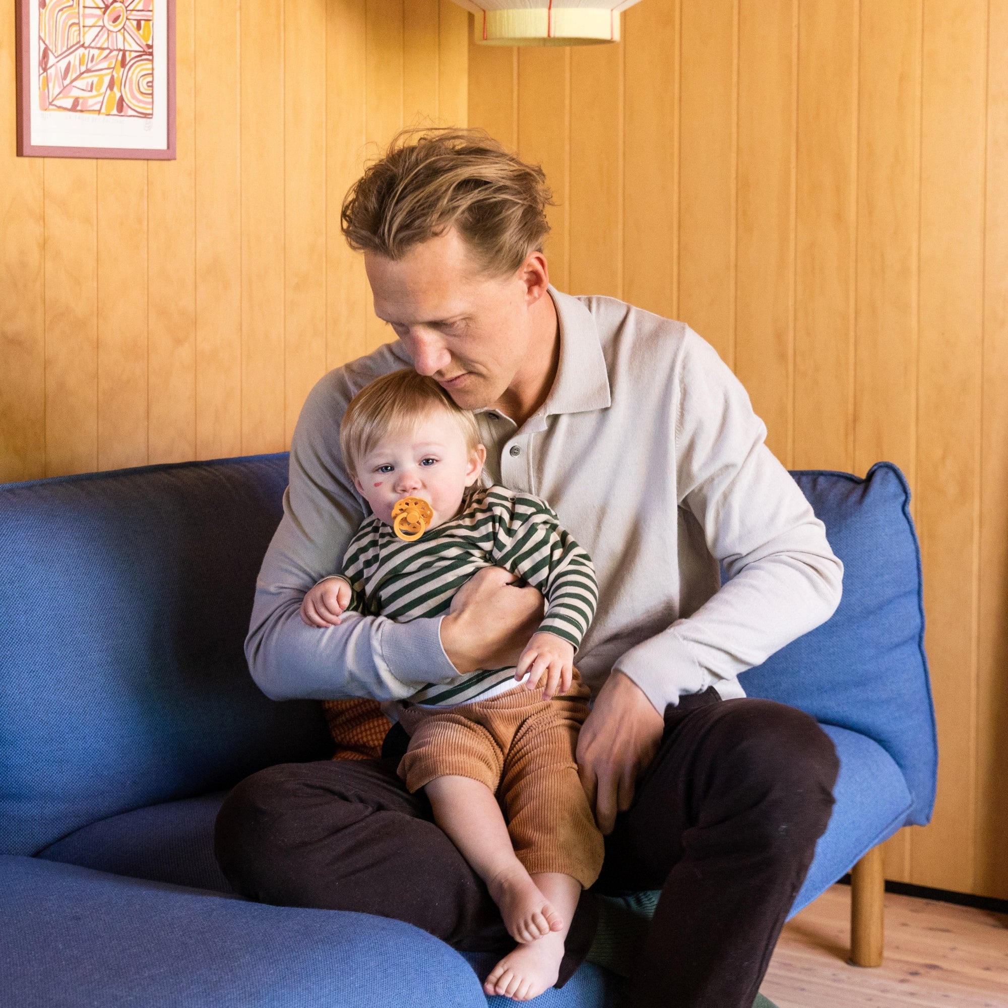 Kisgyerek édesapja ölében ül kék kanapén - sütőtök BIBS Boheme cumi - pippadu