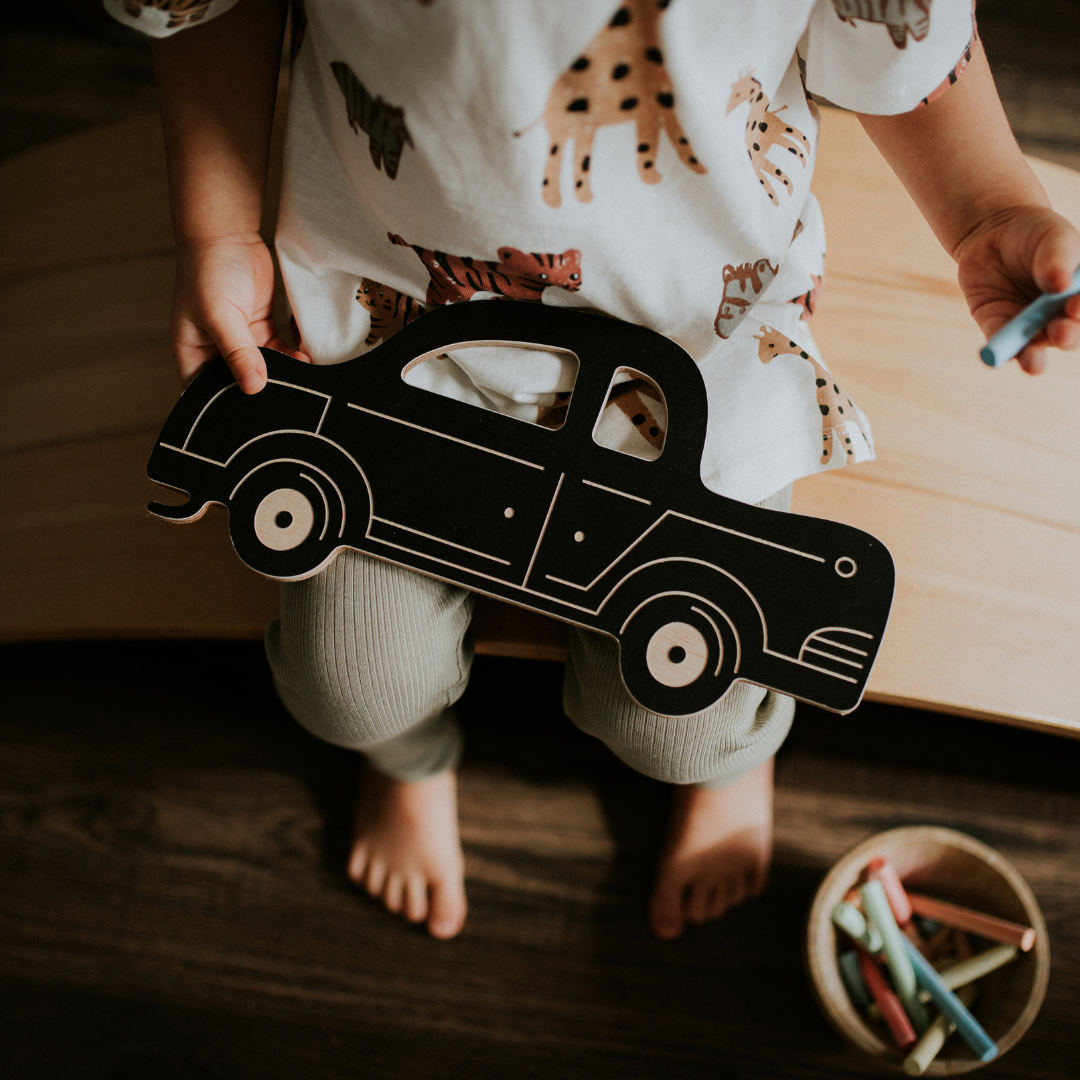 Kisfiú ölében autó formájú rajztábla, amire krétával lehet rajzolni