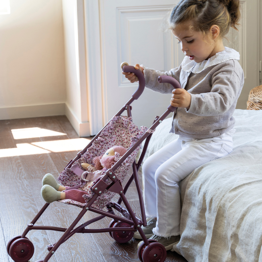 Kislány összecsukható játék babakocsival és plüss babával játszik a gyerekszobában