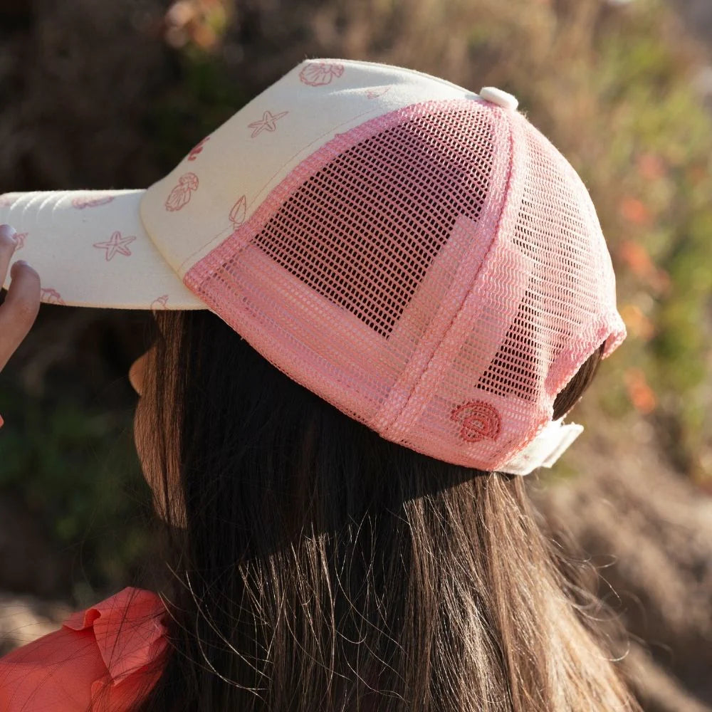 Kislány profilból hálós, kagyló mintás Swim Essentials baseball sapkában.