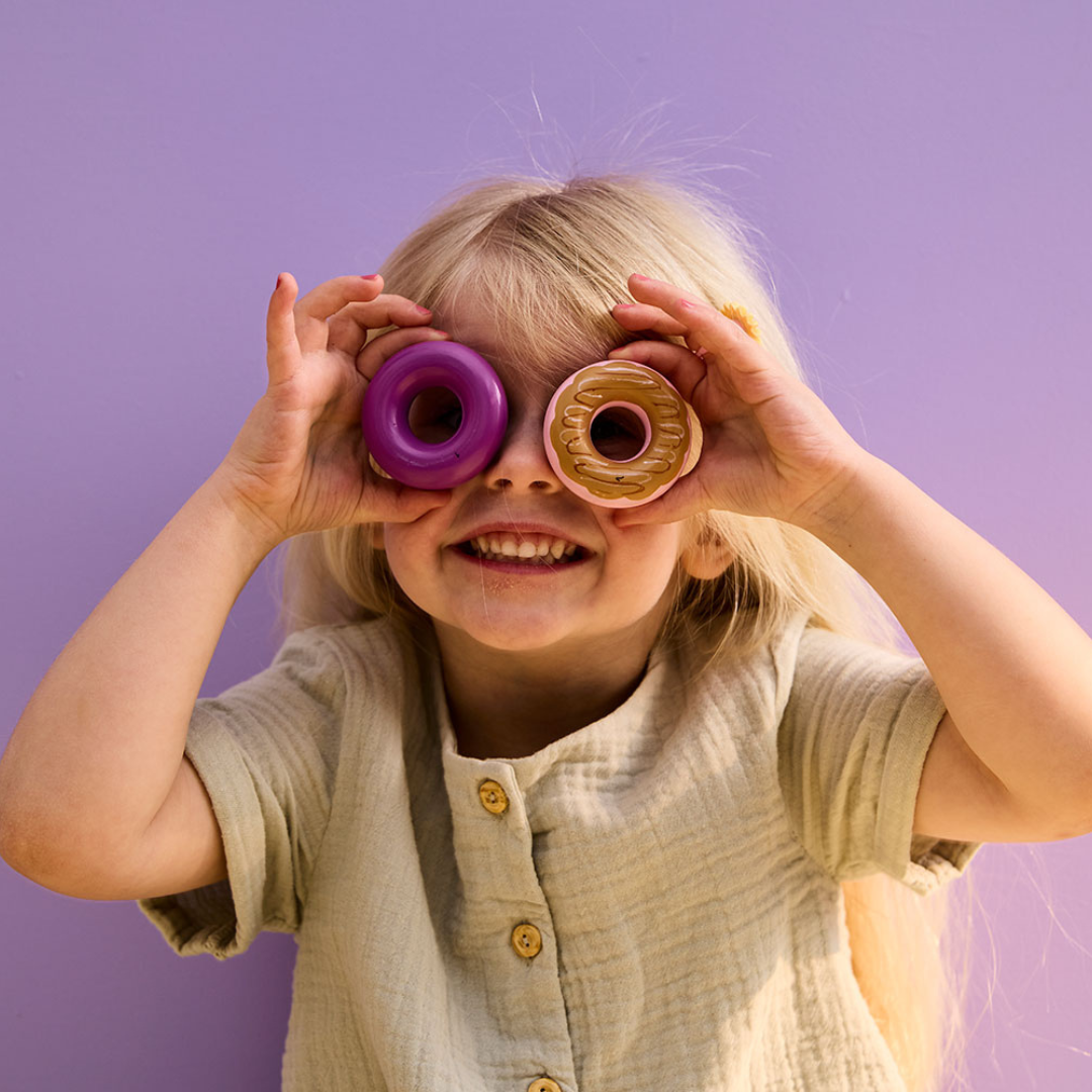 Kislány két Kid's Concept fánkocskát tart a szeme elé játék közben, kreatív és vidám szerepjáték.