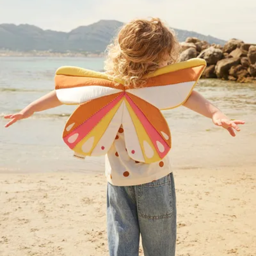 Kislány rózsaszín Kid's Concept pillangó szárnyakkal a parton játszik