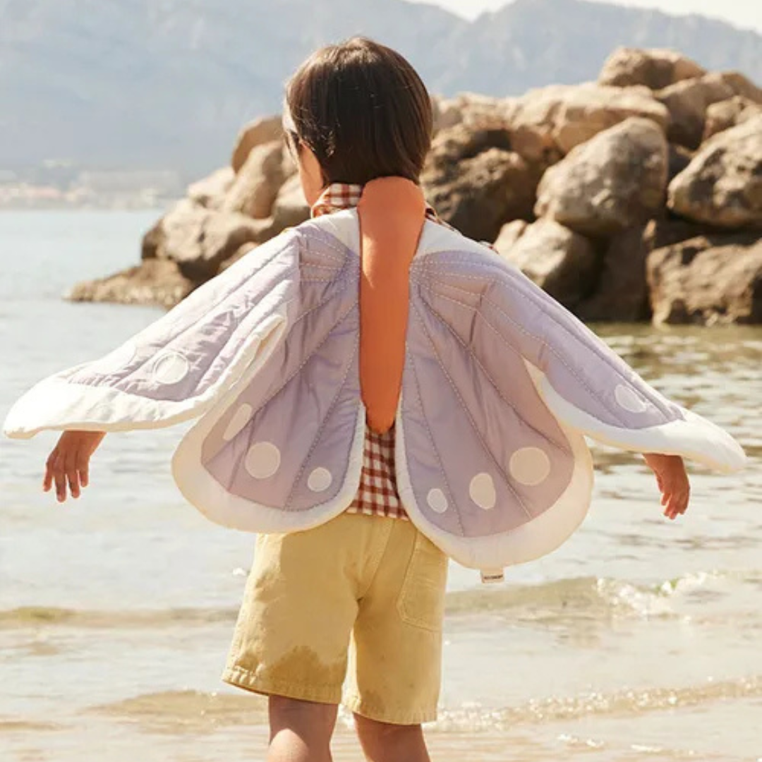 Kisgyermek lila pillangó jelmezben tengerparton – játék közben hátulról fotózva