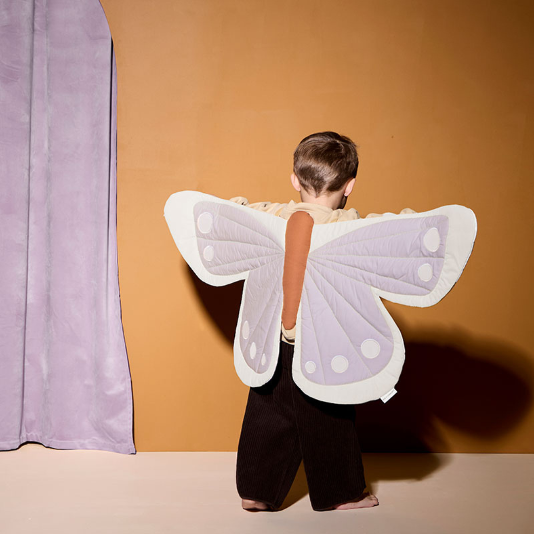 Kisgyermek lila pillangó jelmezben narancssárga háttér előtt – teljes hátulnézetben