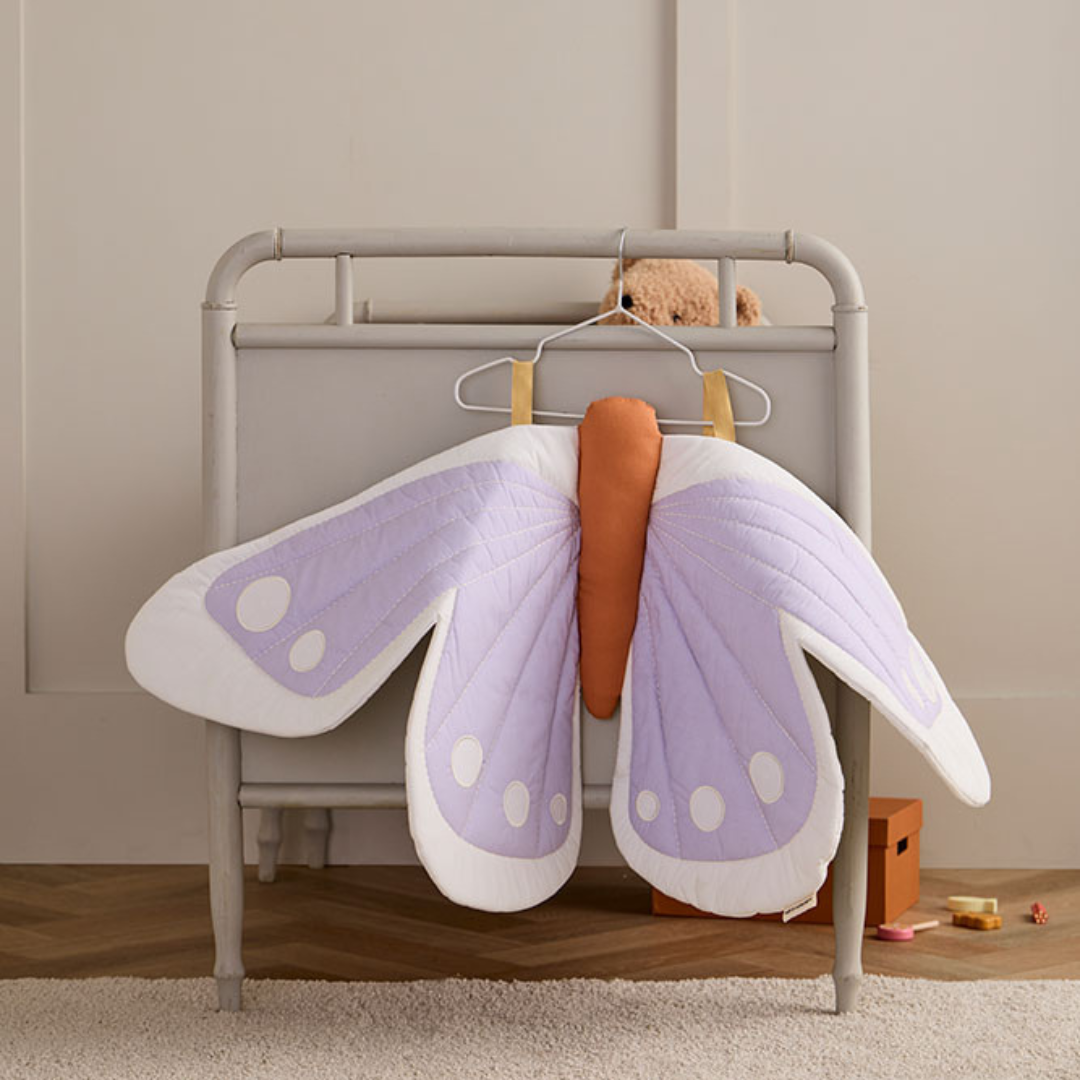Lila gyerek pillangó jelmez vállfán lóg egy gyerekszobában – dekoratív megjelenésben