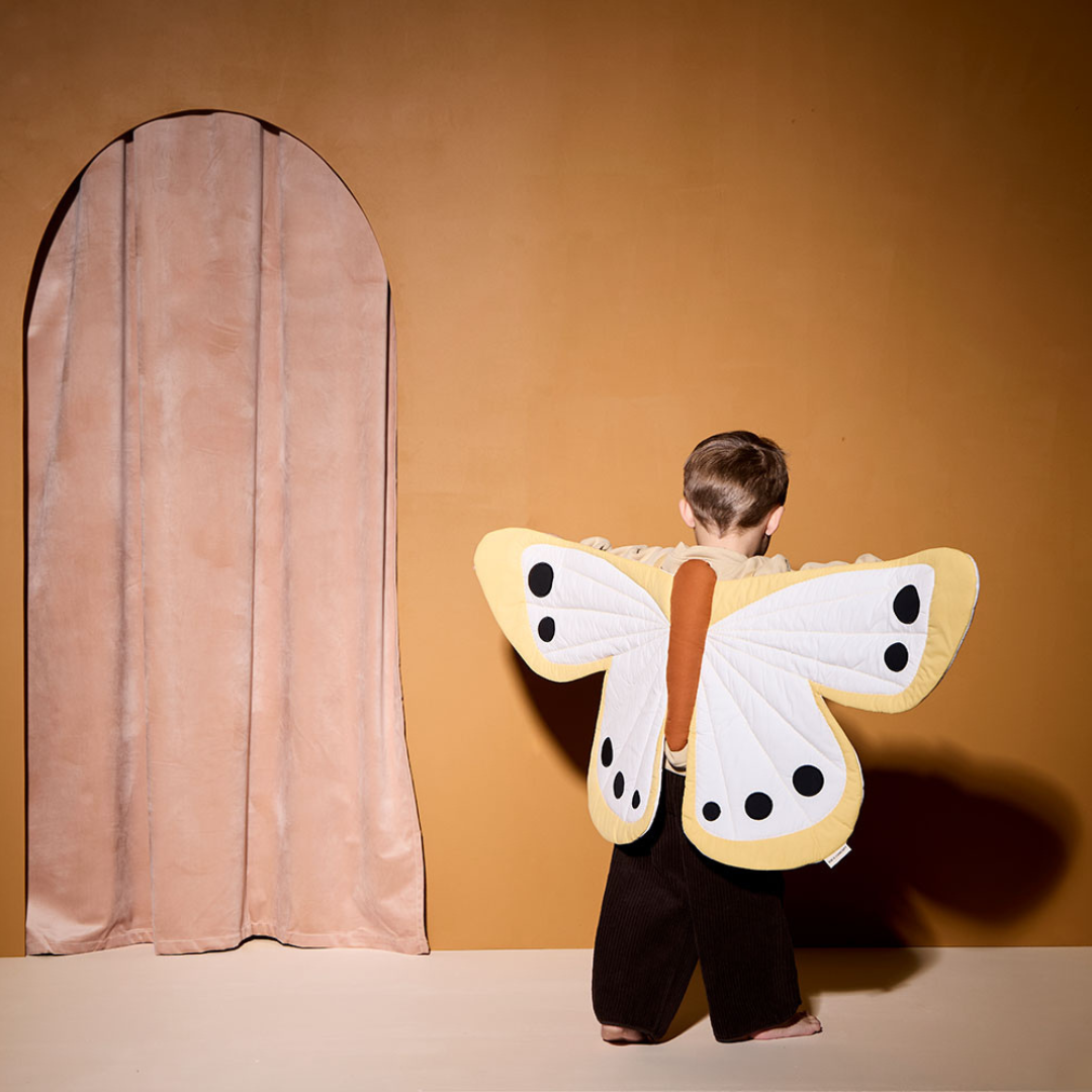 Gyerek sárga pillangó jelmezben, narancs háttér előtt állva