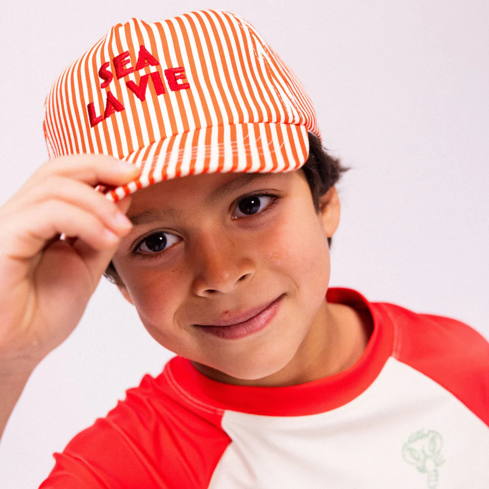Kisfiú piros-fehér csíkos Sea La Vie baseball sapkában és hozzá illő UV-szűrős pólóban.