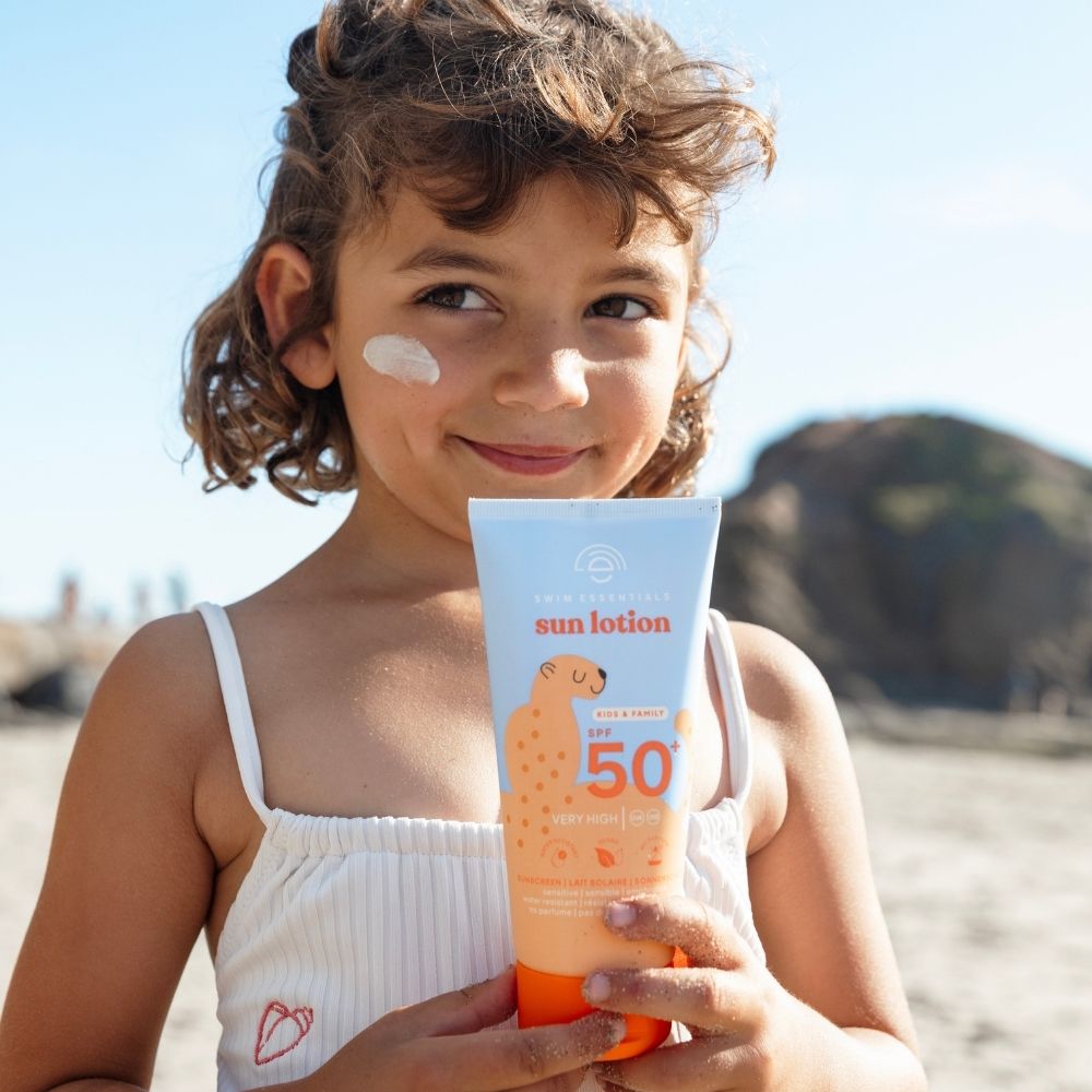 Mosolygó kislány a tengerparton a Swim Essentials SPF 50+ naptejjel, arcán egy pötty krémmel.