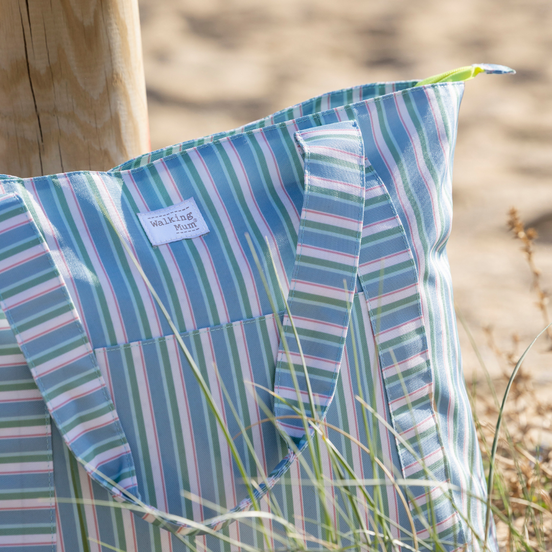 Közelkép a Walking Mum zöld-kék csíkos strandtáskáról a tengerparti homokban