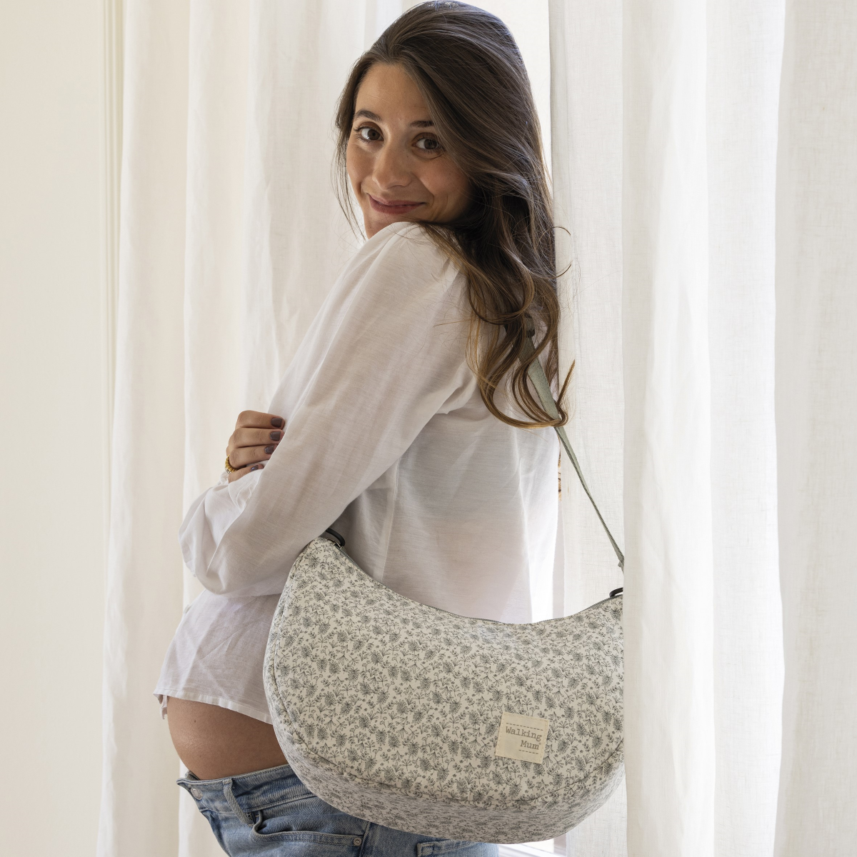 Kismama gondola menta színű pelenkázó táskával a vállán a kamera név az ablak előtt állva