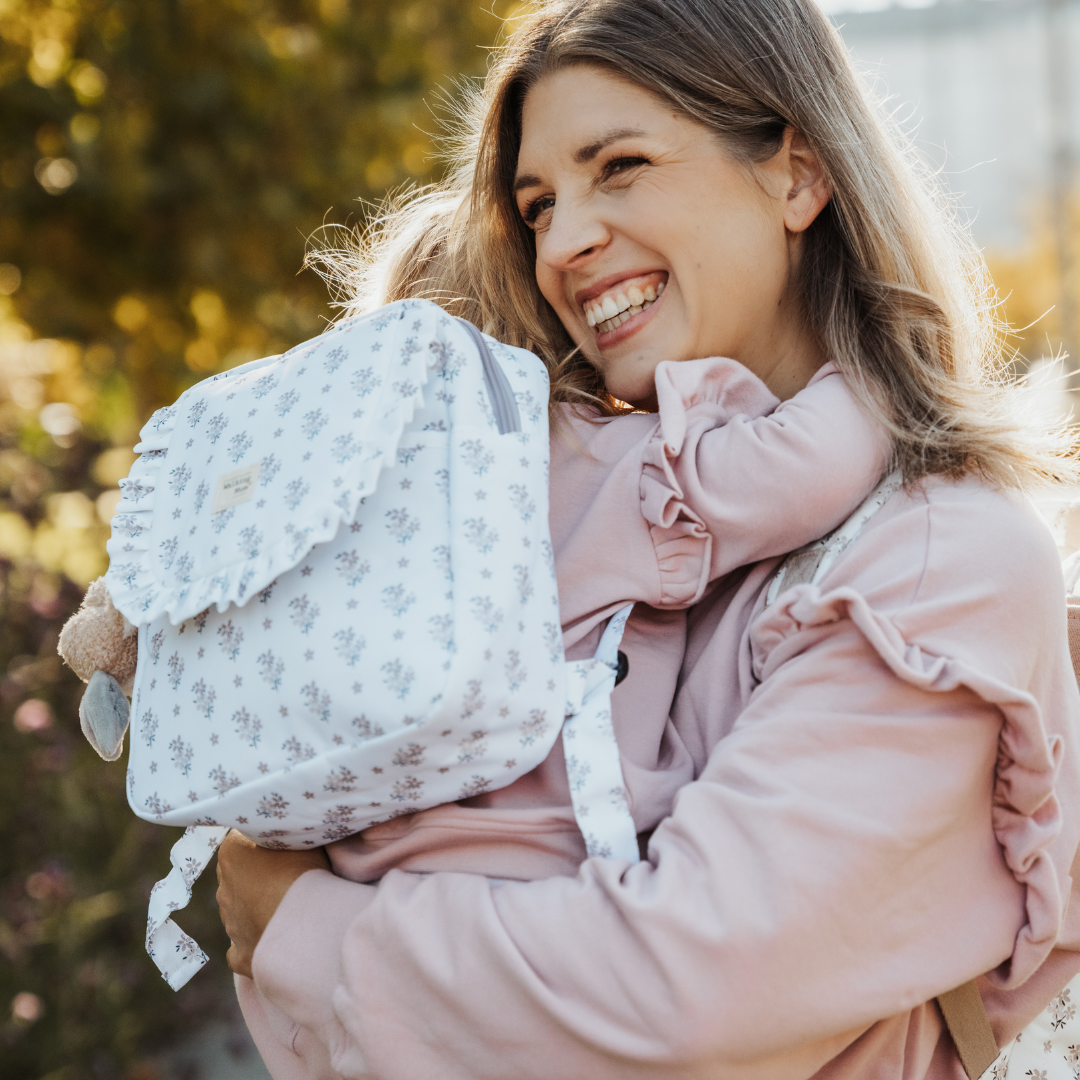 Kislány és anyukája ölelik egymást - kislányon virágos gyerek hátizsák patentos záródással, állítható vállpántokkal