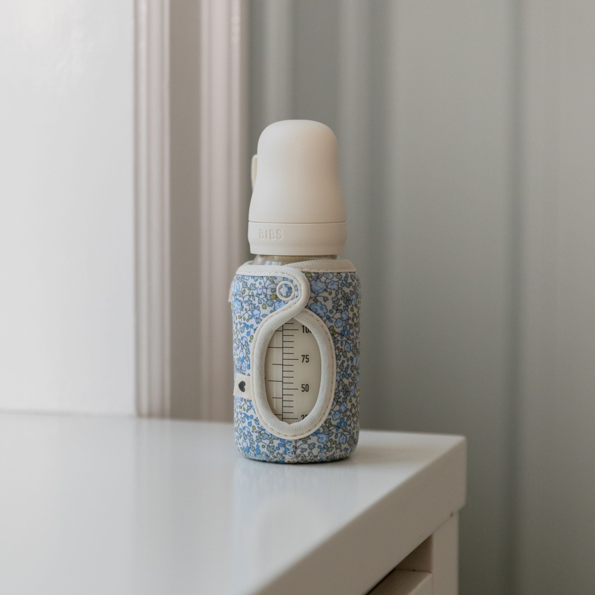 Cumisüveg virágos mintás tokban polcon - pippadu