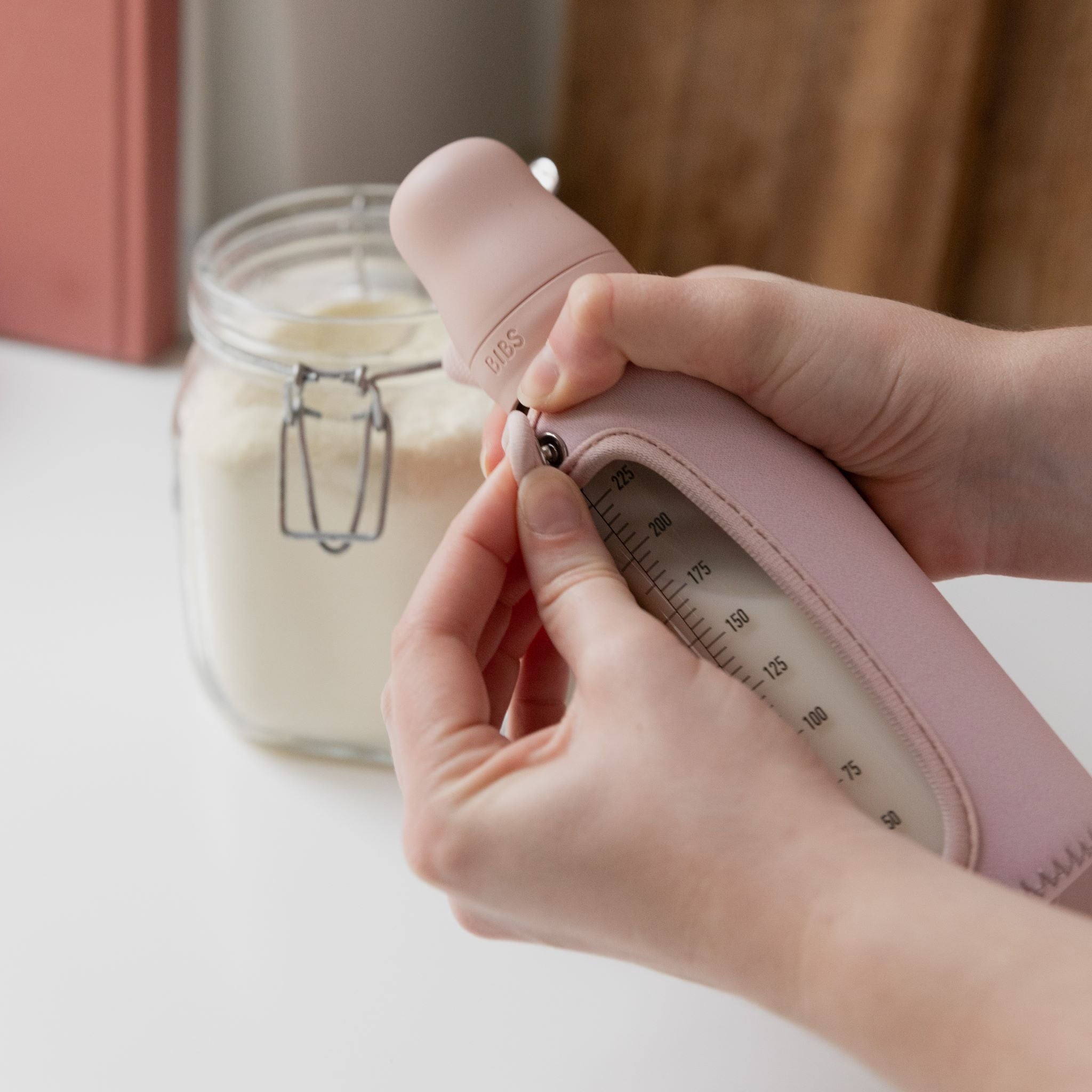 Édesanya kezében patenttal rögzíthető BIBS cumisüveg tok púderrózsaszín színben - pippadu