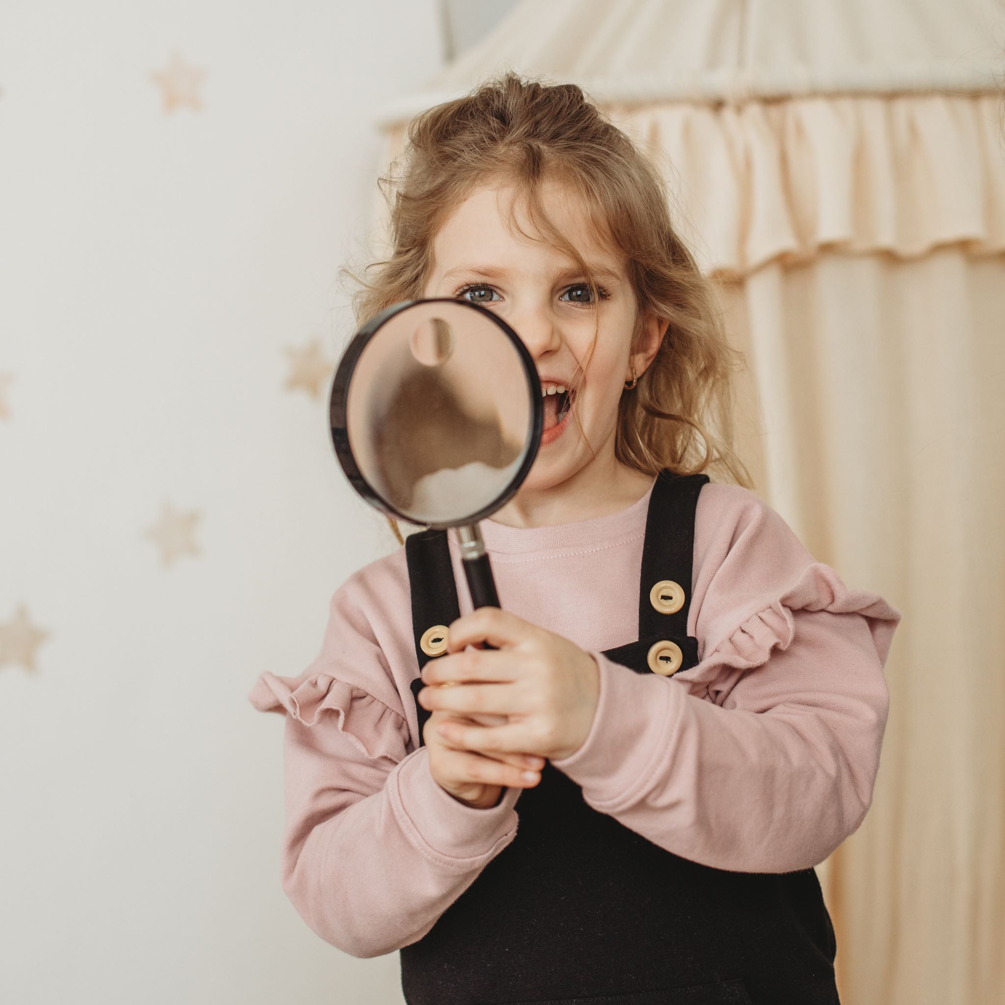 Kislány nagyítóval kamerába néz fodros szilvarózsa pulóverben - pippadu