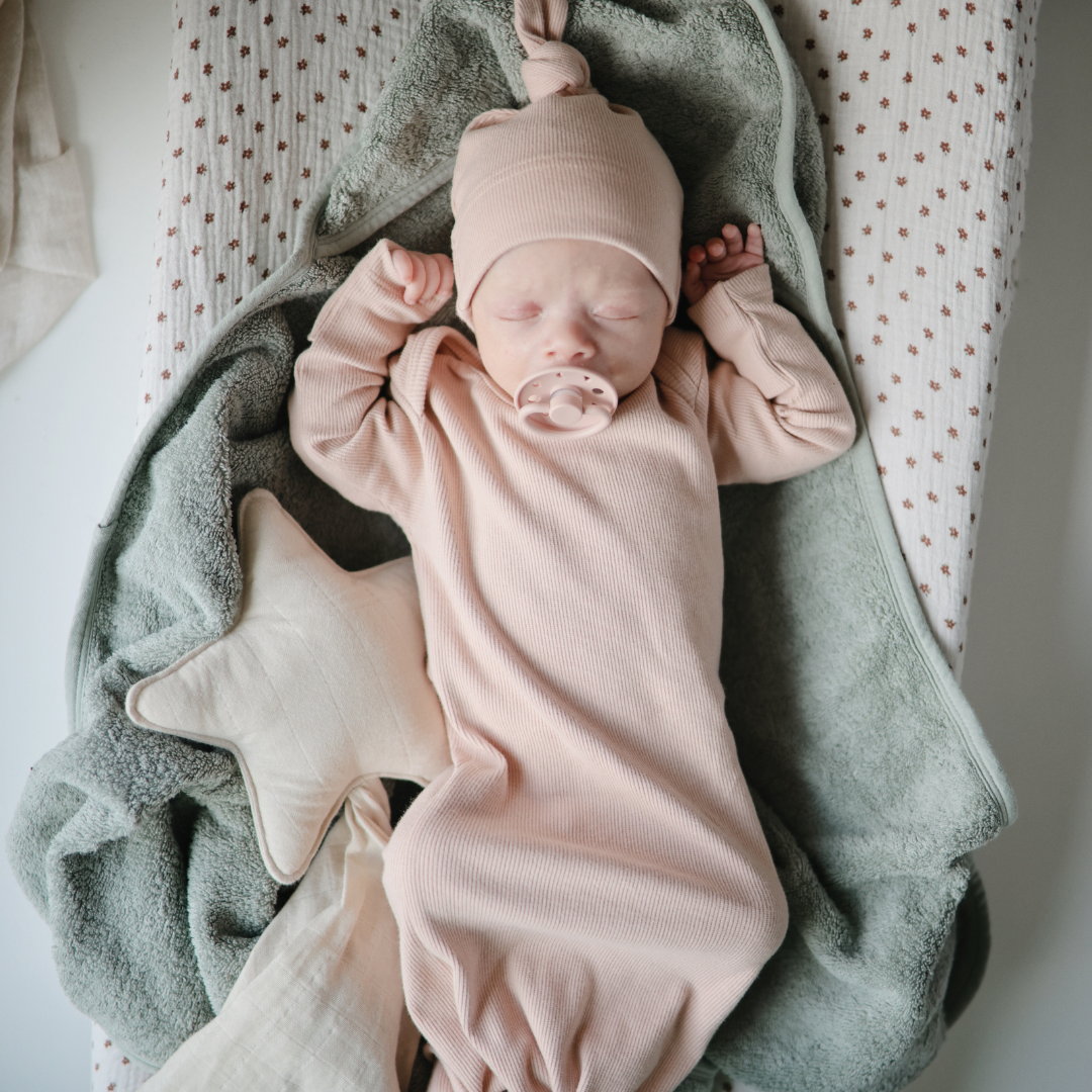 Kisbaba pelenkázón pihen Mushie csillag szundikendővel az oldalán, cumival a szájában