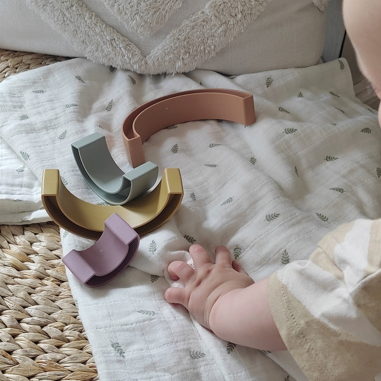 Kisgyerek szivárvány építővel játszik muszlin pólyán