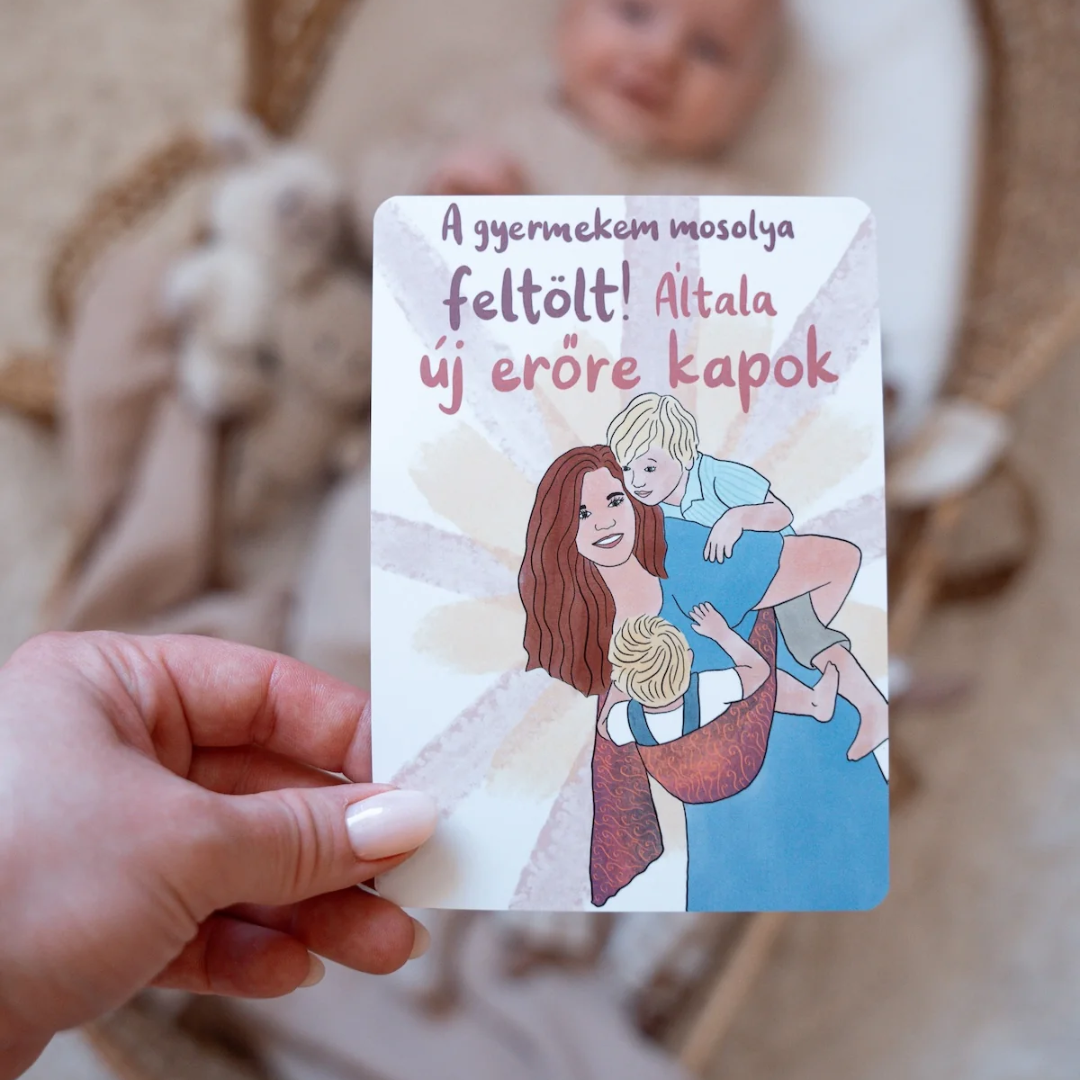Kézben tartott Modern Goddess anyaság kártya A gyermekem mosolya feltölt felirattal, háttérben egy kisbabával.