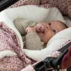 Kisbaba az ujját szopizza, miközben a virágmintás babafészekben pihen a babakocsiban