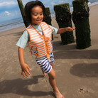 Kisgyermek a tengerparton Bluey mintás Swim Essentials úszómellényben, biztonságos csattal.