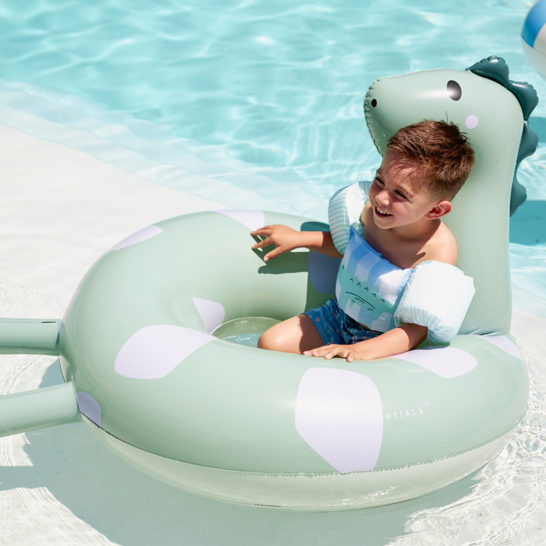 Kisgyermek pancsol a medencében a Swim Essentials hosszú nyakú dínó úszógumijával.