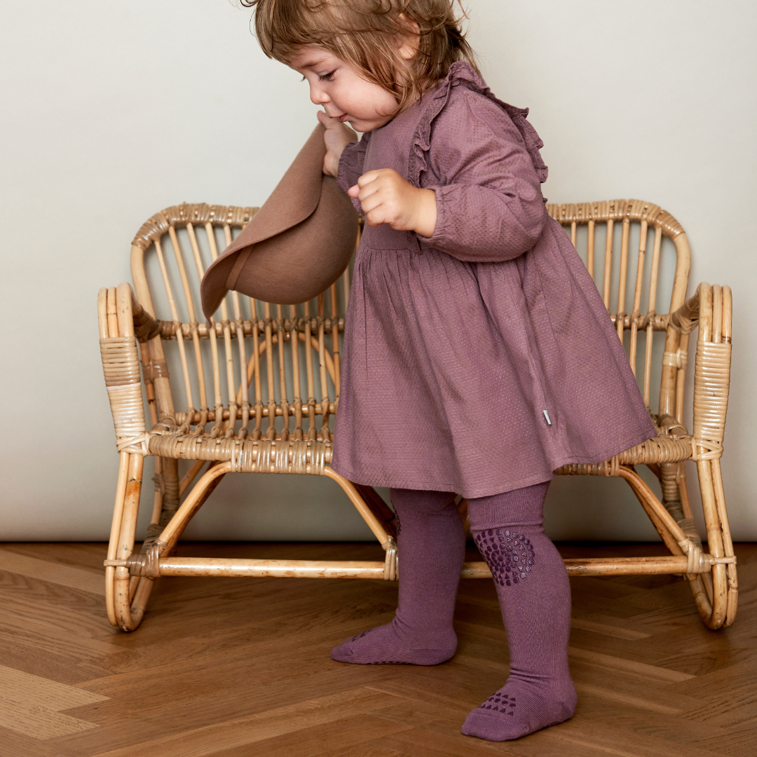 Kislány GobabyGo szilva csúszásgátlós harisnyanadrágban egy kalapot fog a kezében