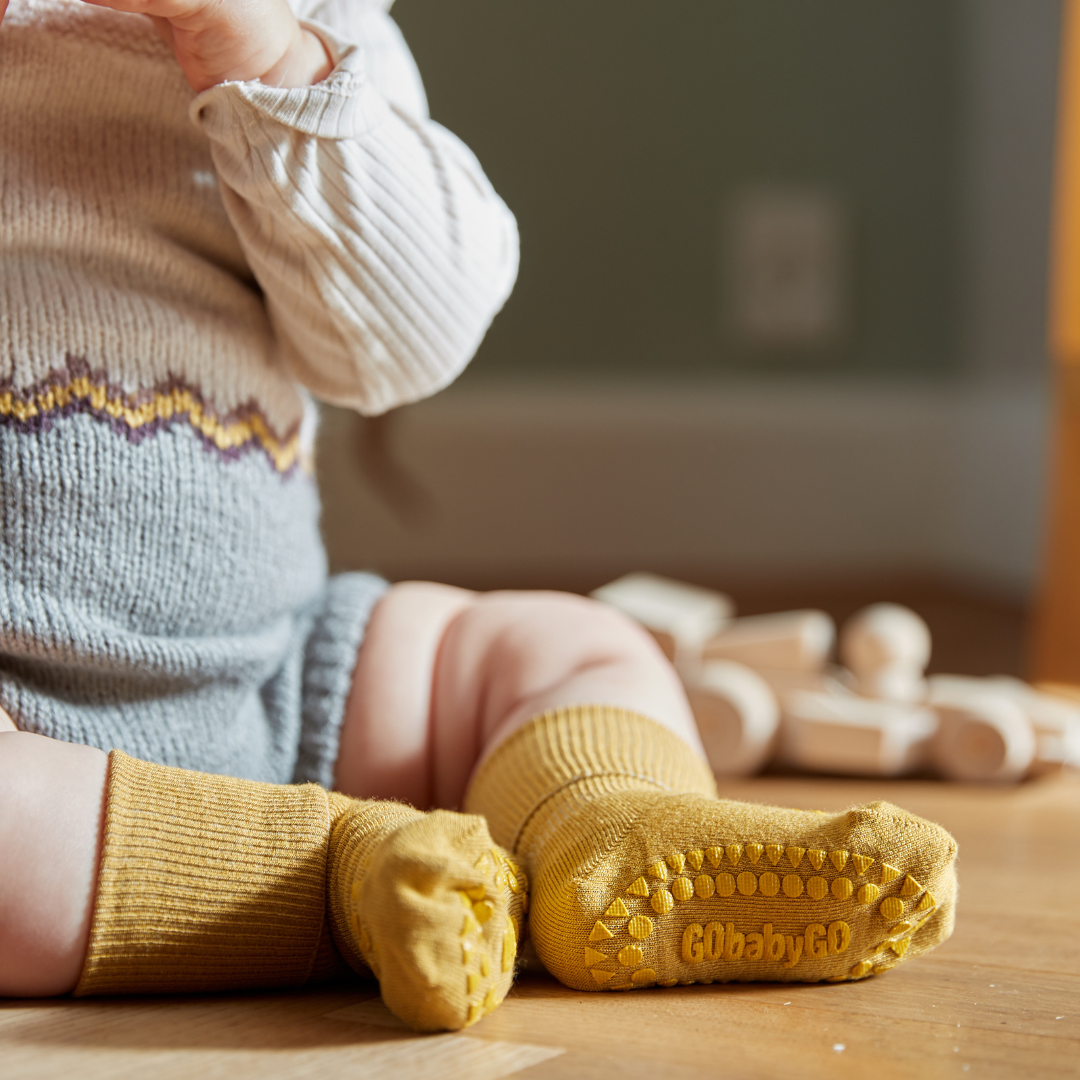 Kisbaba a földön ül csúszásgátlós bambusz zoknival a lábán