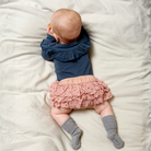 Kislány hason fekszik az ágyon rózsaszín szoknyában és szürke melange csúszásgátlós bambusz zokniban