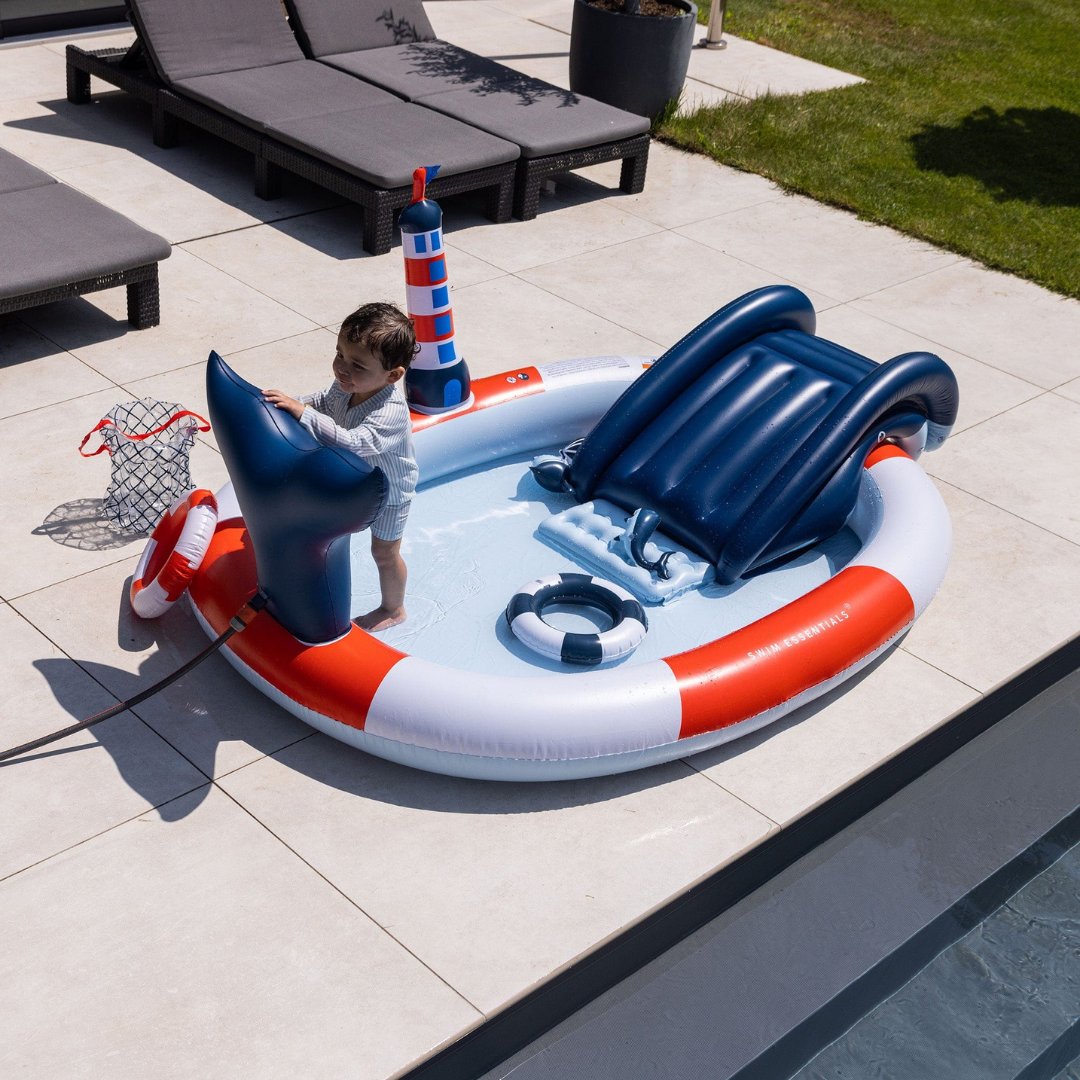 Gyermek játszik a medencében a felfújható világítótorony és a spriccelő bálnafarok mellett.