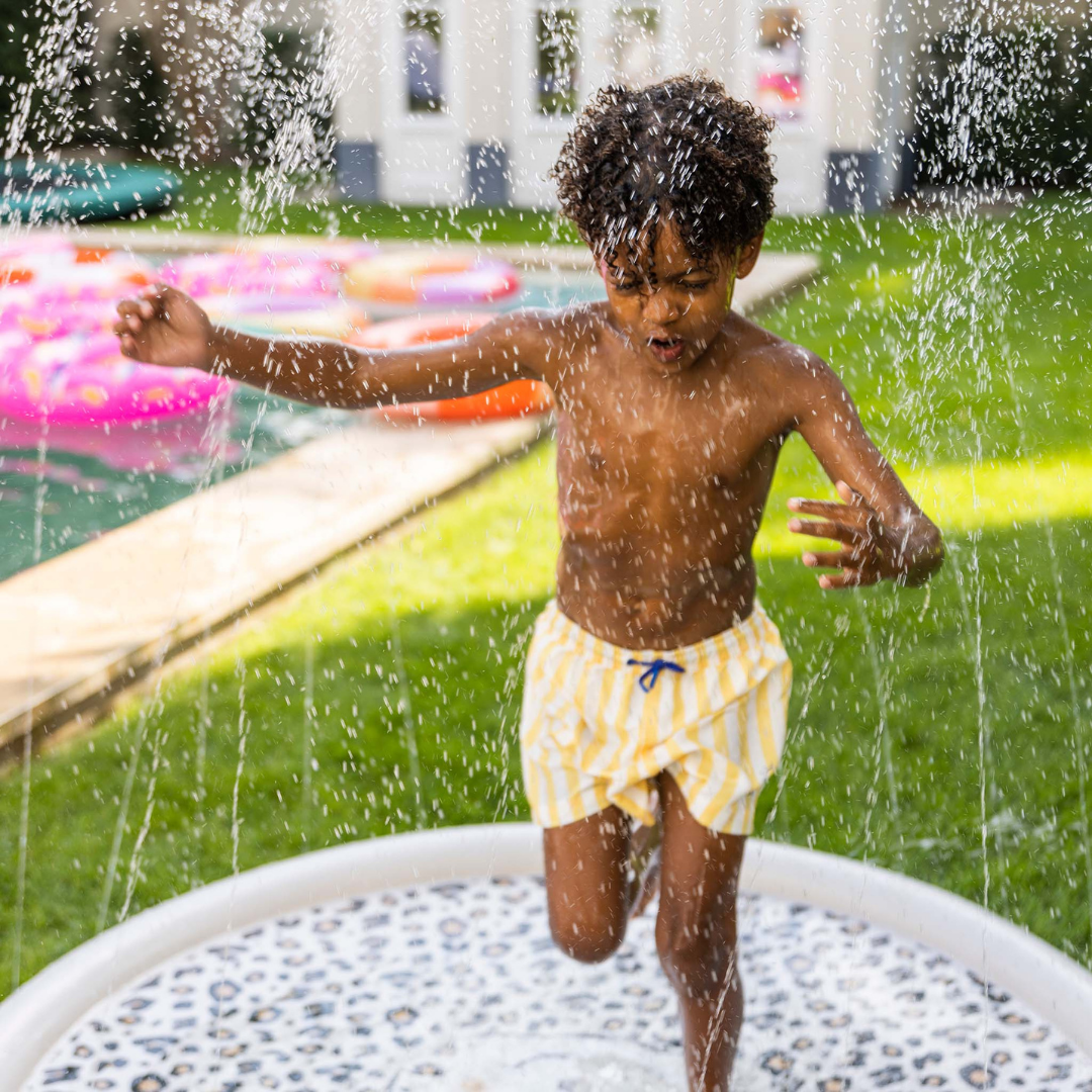 Gyermek élvezi a kerti locsolóra csatlakoztatott szökőkút pancsoló hűsítő vízsugarait.