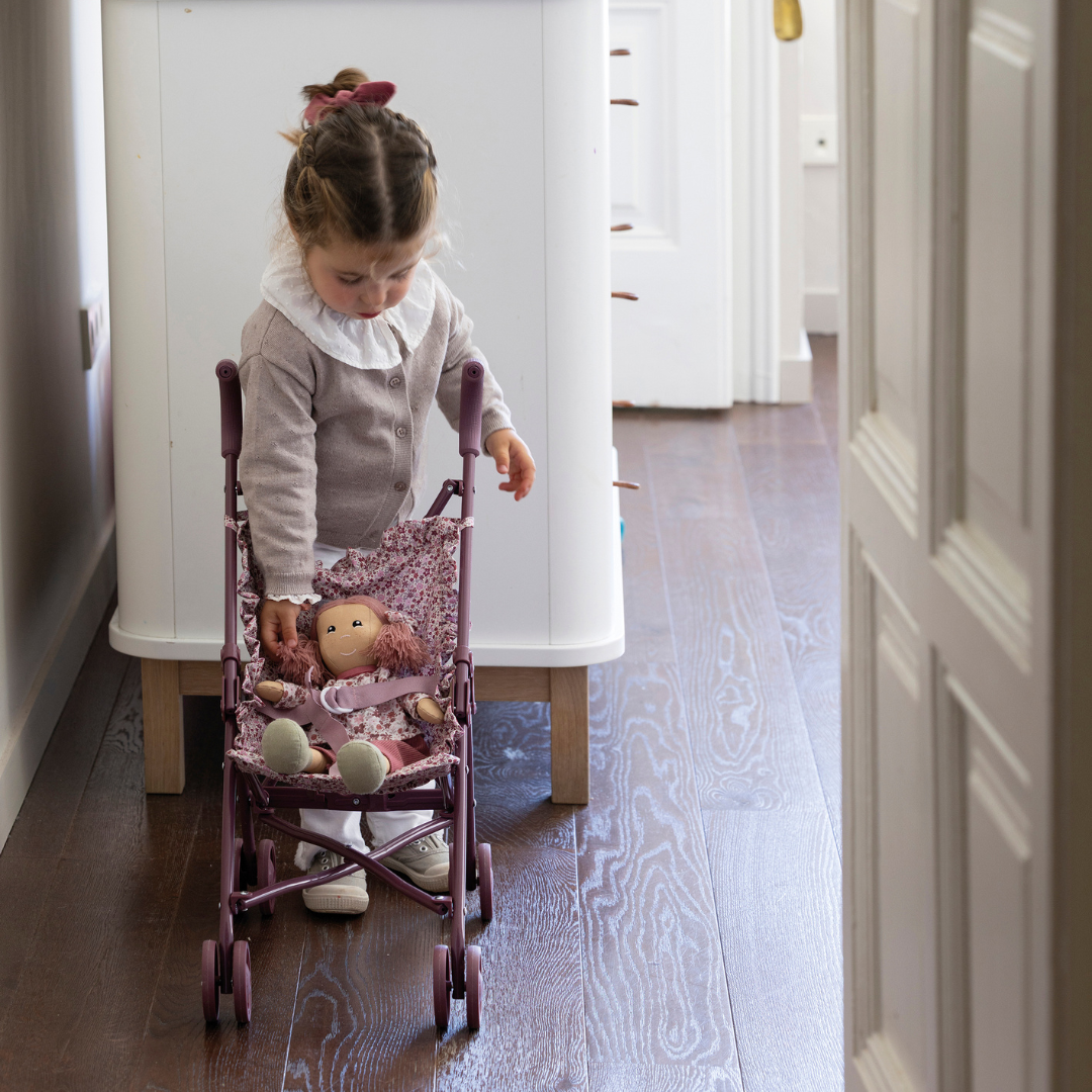 Kislány a szobájában virágmintás játék babakocsit tol, plüss babával