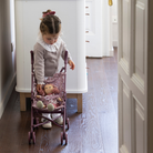 Kislány a szobájában virágmintás játék babakocsit tol, plüss babával