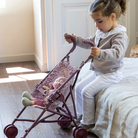 Kislány összecsukható játék babakocsival és plüss babával játszik a gyerekszobában