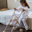 Kislány összecsukható játék babakocsival játszik az ágyon ülve