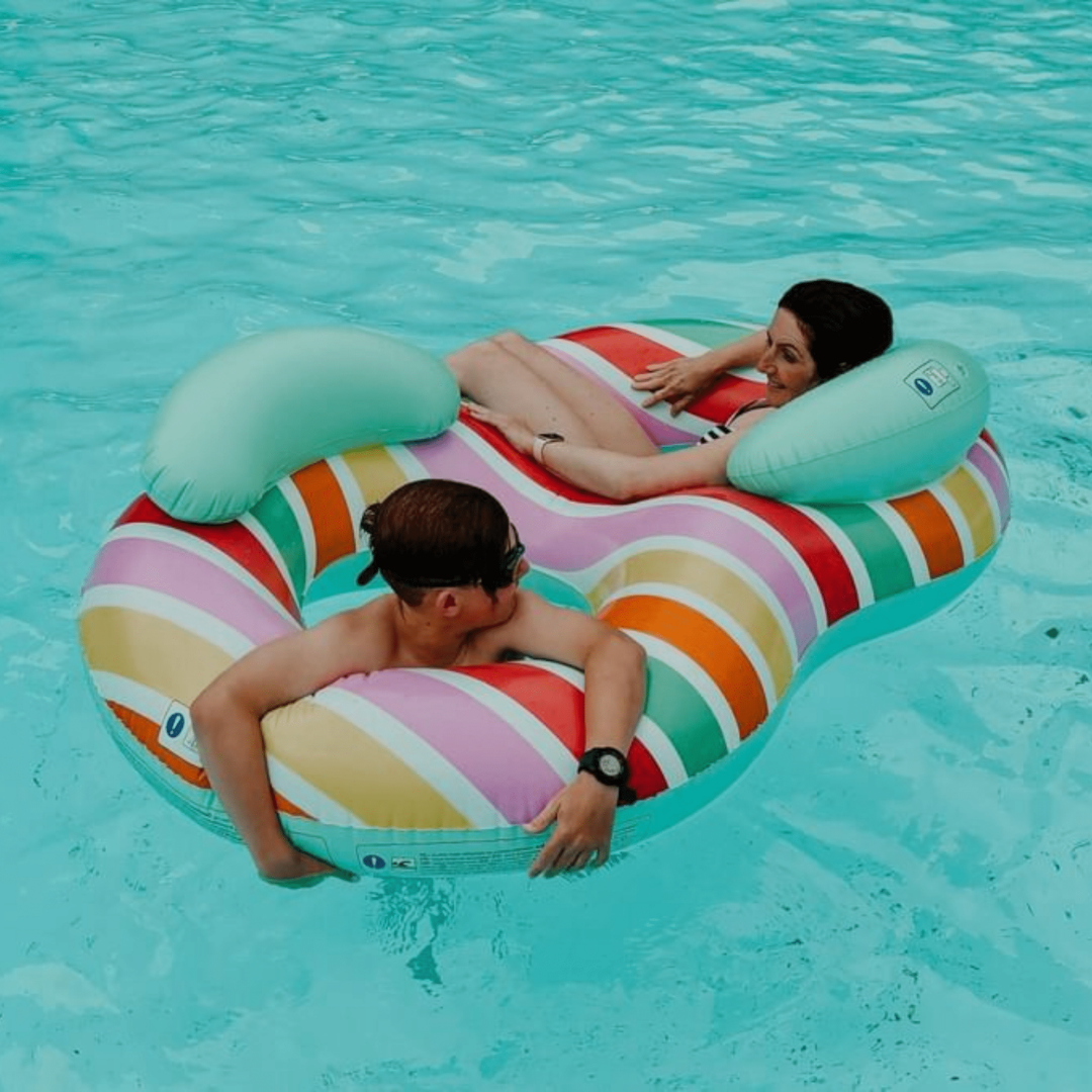Két ember pihen a Swim Essentials színes, kétszemélyes úszógumiján a medencében.
