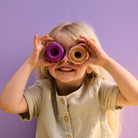 Kislány két Kid's Concept fánkocskát tart a szeme elé játék közben, kreatív és vidám szerepjáték.