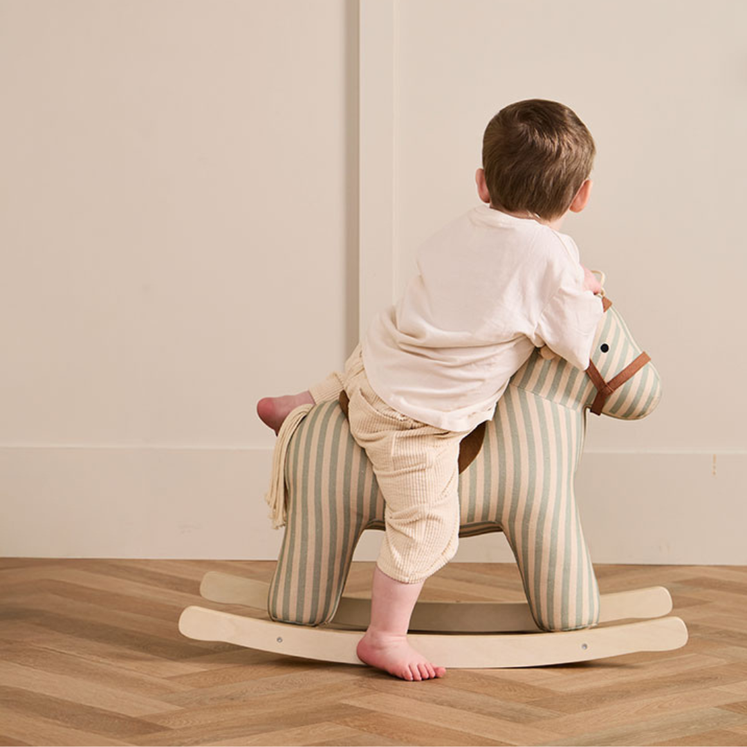 Kisgyermek játszik a Kid's Concept Sam csíkos hintalovon, skandináv stílusú gyerekszobában