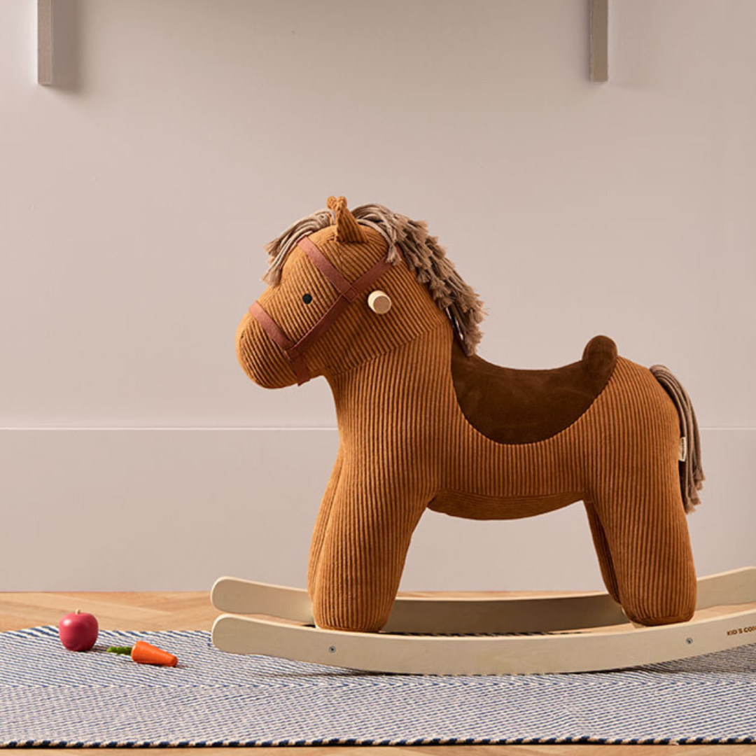 A Kid's Concept Vera barna kordbársony hintaló egy skandináv stílusú gyerekszobában, csíkos szőnyegen állva, játékok mellett a Pippadu kínálatából