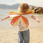 Kislány rózsaszín Kid's Concept pillangó szárnyakkal a parton játszik