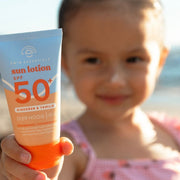 Mosolygó kislány a tengerparton, orrán egy pötty naptejjel, kezében a Swim Essentials naptejjel.