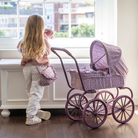 Kislány babával a kezében kinéz az ablakon - vállán fodros, virág mintás táska, mellette klasszikus játék babkocsi nagy kerekekkel, állítható kupolával