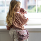 Kislány fodros válltáskával és plüss babával áll az ablak előtt - a fodros táska a klasszikus játék babakocsihoz tartozik