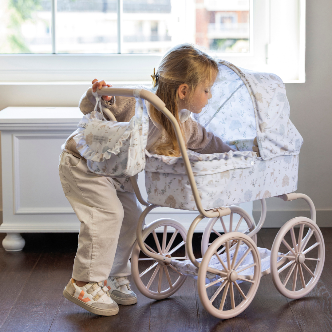 Kislány játszik klasszikus játék babakocsival, amihez hozzá illő válltáska is tartozik