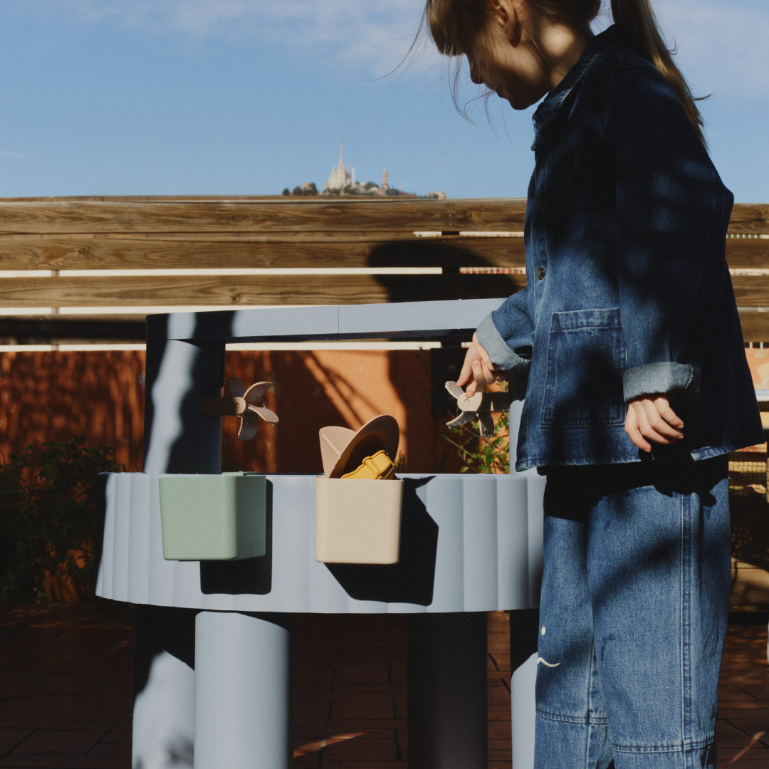 Gyerek játszik a kék homokozó és vizező játékasztallal kültéren