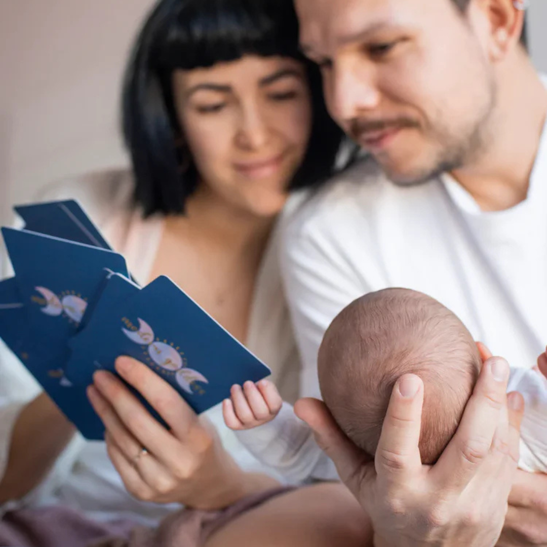 Anya és apa az újszülött babával a Modern Goddess apakártyákat nézik.