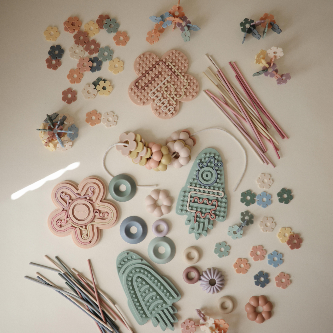 Mushie játékok nagy kollekció flatlay – több Mushie fejlesztőjáték és matató bézs alapon