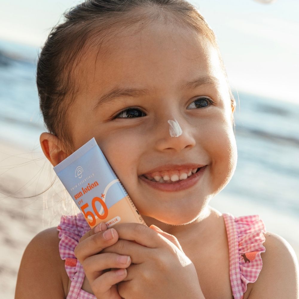 Kislány mutatja a Swim Essentials 50 ml-es, érzékeny bőrre kifejlesztett naptejét a strandon.