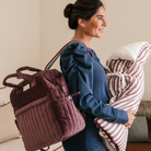 Édesanya fél vállán bársony pelenkázó hátizsák állítható nagyságú oldalzsebekkel, kezében csíkos babafészek kisbabának