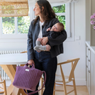 Édesanya kezében kisbabával bársony pelenkázó táskáját fogja a kezében, a konyhában állva