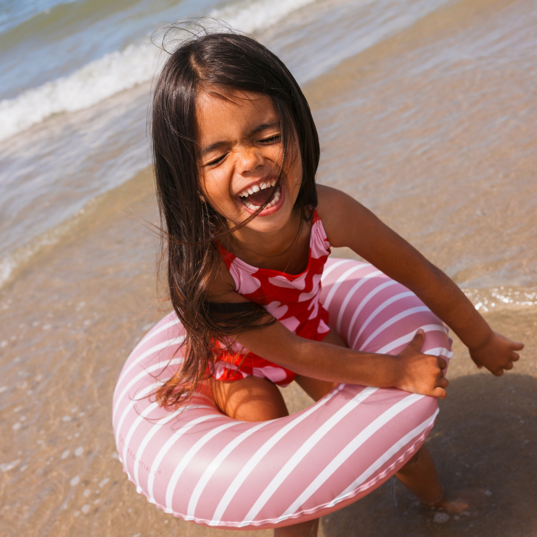 Kislány a tengerpartjon a Swim Essentials stílusos rózsaszín-fehér csíkos úszógumijával.