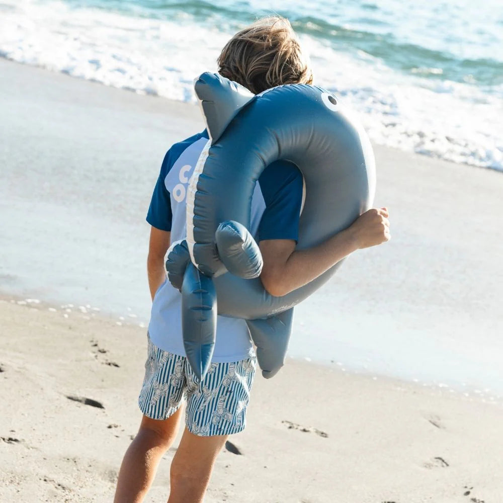 Kisfiú sétál a tengerparton a sötétkék bálnás Swim Essentials úszógumival.